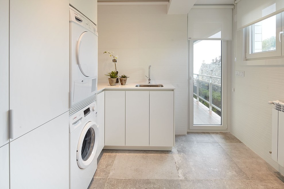 Foto de cuarto de lavado en L contemporáneo de tamaño medio con fregadero de un seno, armarios con paneles lisos, puertas de armario blancas, paredes blancas y lavadora y secadora apiladas