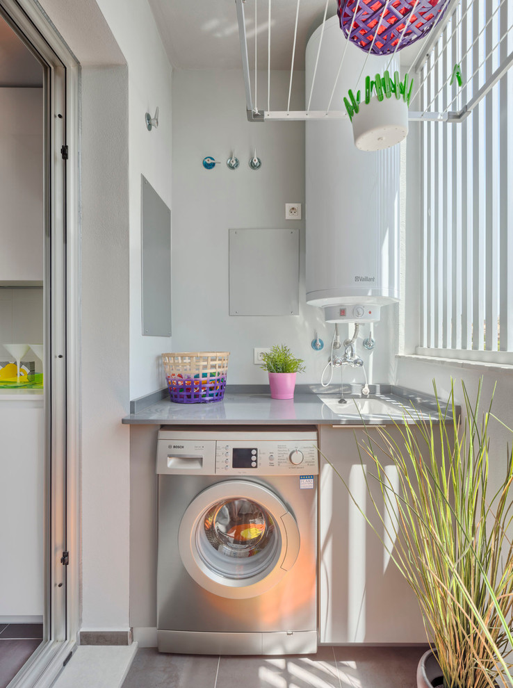 Bild på en mellanstor eklektisk grå linjär grått tvättstuga enbart för tvätt, med en undermonterad diskho, släta luckor, grå skåp, vita väggar och en tvättmaskin och torktumlare bredvid varandra