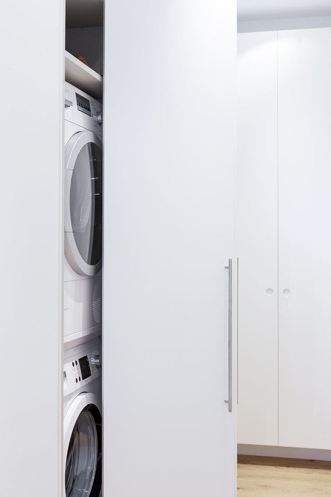 Minimalistisk inredning av en liten liten tvättstuga, med släta luckor, vita skåp, vita väggar och en tvättpelare