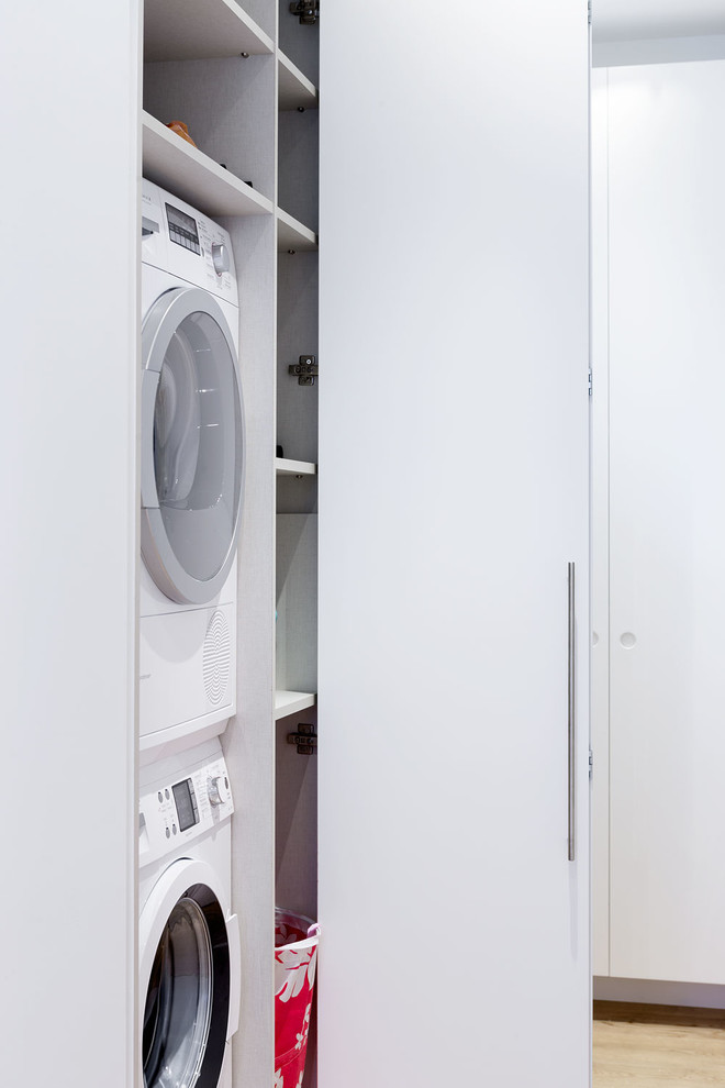 Kleiner Skandinavischer Hauswirtschaftsraum mit Waschmaschinenschrank, flächenbündigen Schrankfronten, weißen Schränken und Waschmaschine und Trockner gestapelt in Sonstige