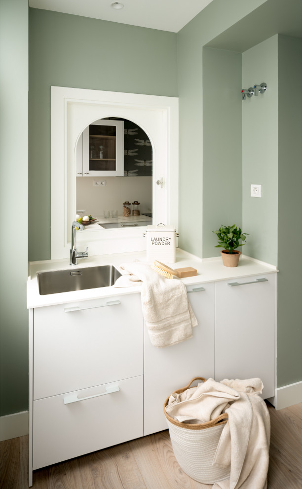 Inspiration för mellanstora skandinaviska linjära vitt tvättstugor enbart för tvätt, med en undermonterad diskho, släta luckor, vita skåp, bänkskiva i kvarts, gröna väggar, laminatgolv och tvättmaskin och torktumlare byggt in i ett skåp