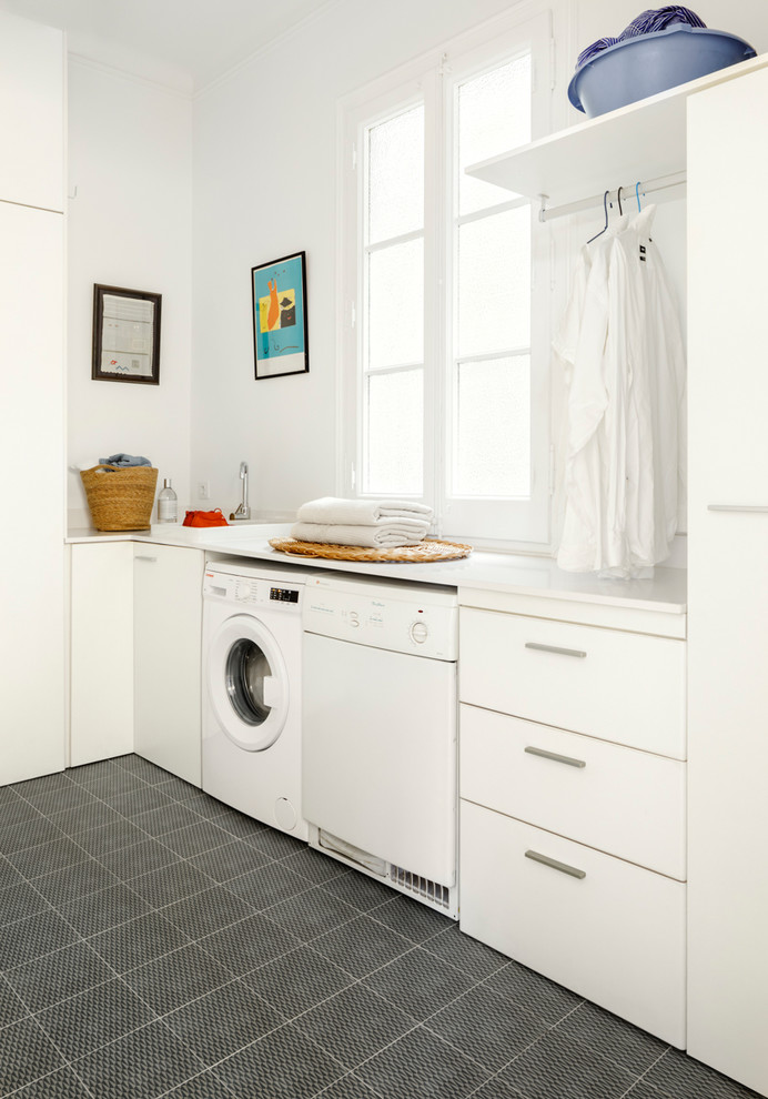 Moderne Waschküche in L-Form mit weißen Schränken, weißer Wandfarbe, Porzellan-Bodenfliesen, Waschmaschine und Trockner nebeneinander und grauem Boden in Barcelona