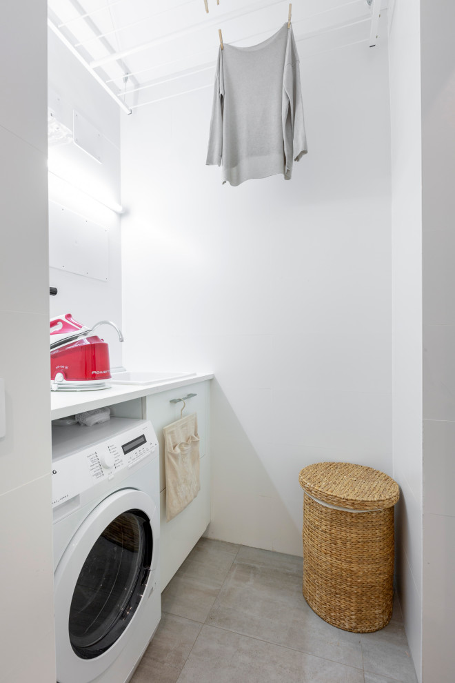 Inredning av en modern liten vita linjär vitt tvättstuga enbart för tvätt, med släta luckor, vita skåp, laminatbänkskiva, vita väggar, klinkergolv i keramik, grått golv och en nedsänkt diskho