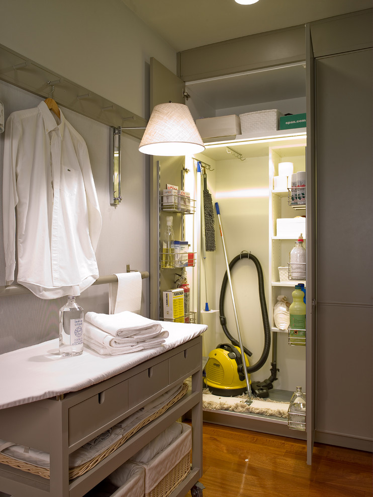 Imagen de cuarto de lavado lineal clásico pequeño con armarios con paneles lisos, paredes beige, suelo de madera en tonos medios y puertas de armario grises
