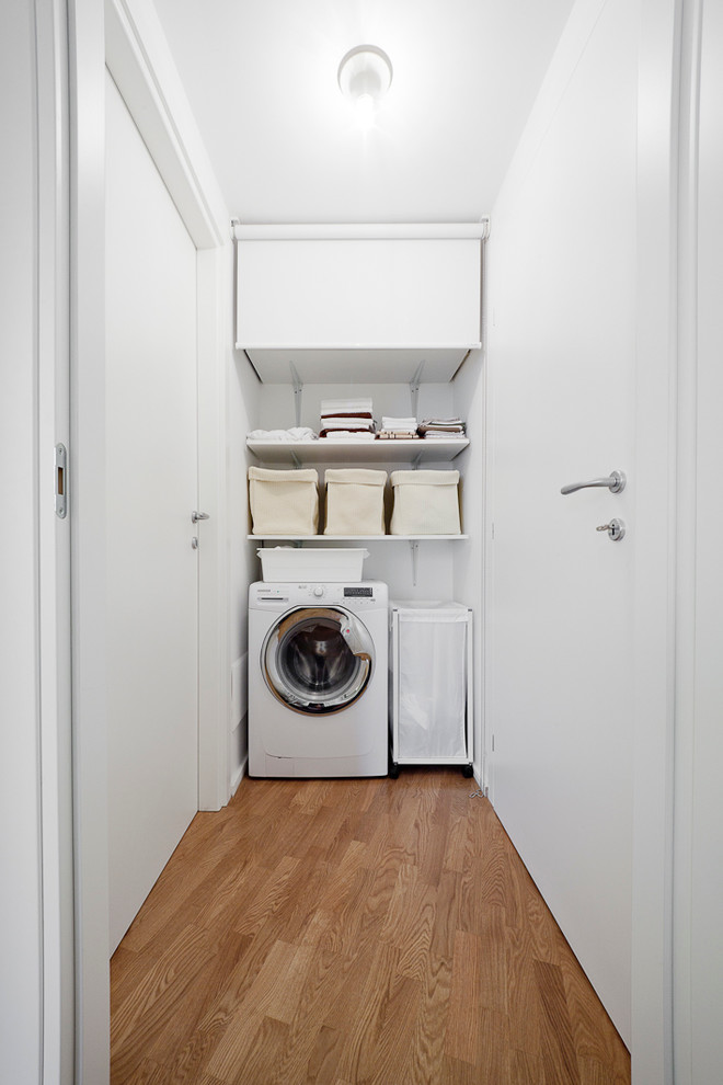 Réalisation d'une buanderie linéaire design dédiée avec un mur blanc et un sol en bois brun.