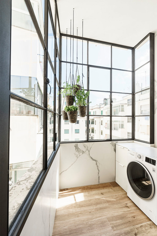 Foto di una piccola sala lavanderia minimal con ante lisce, ante bianche, pareti bianche, pavimento in legno massello medio, lavatrice e asciugatrice affiancate e pavimento marrone