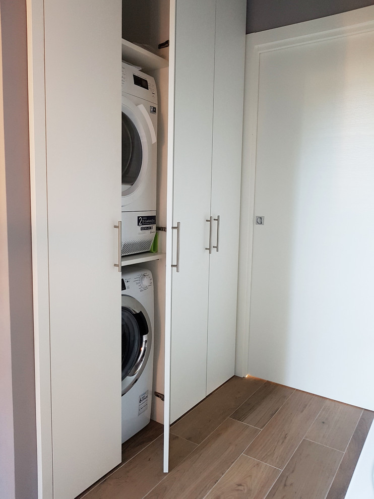 Esempio di una piccola sala lavanderia minimal con ante lisce, ante bianche, pareti grigie, pavimento in gres porcellanato, lavatrice e asciugatrice a colonna e pavimento marrone
