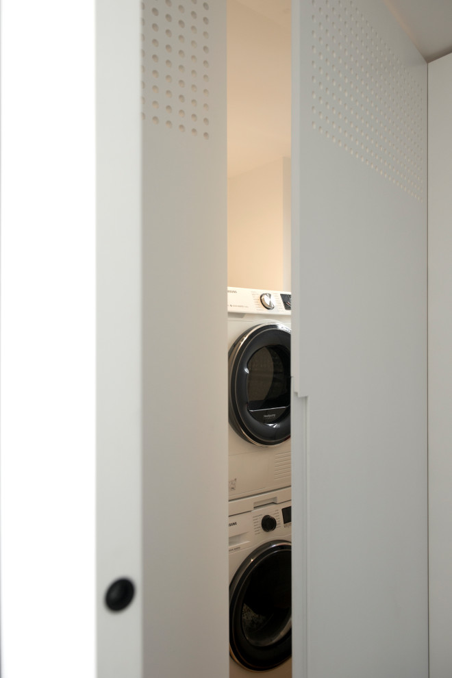 Immagine di una piccola lavanderia multiuso contemporanea con nessun'anta, ante bianche, pareti bianche, pavimento in legno massello medio, lavatrice e asciugatrice a colonna e pavimento marrone