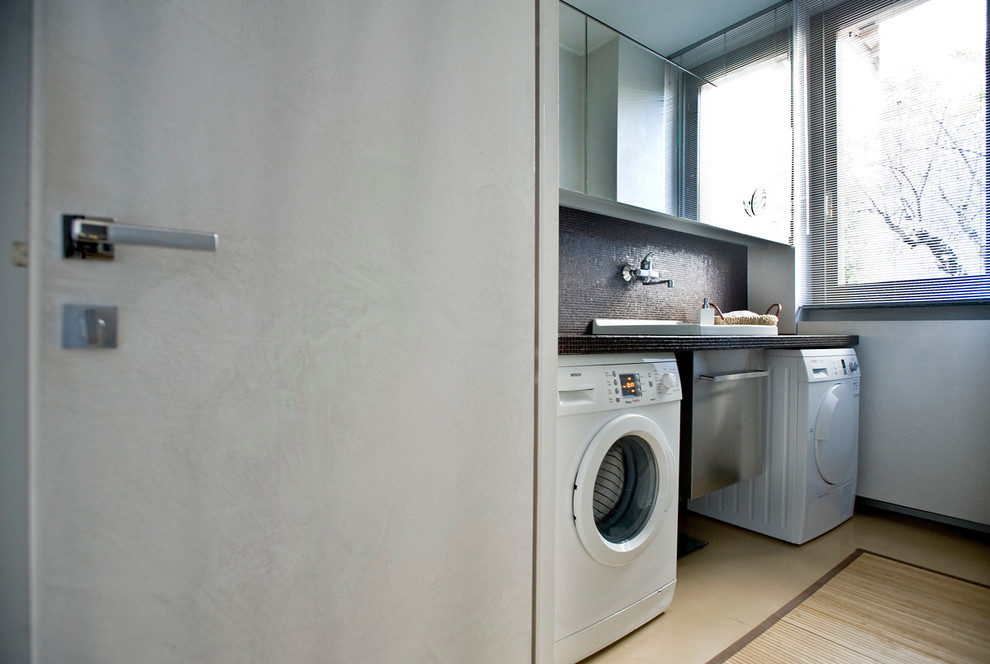 Modern inredning av en tvättstuga, med luckor med glaspanel, vita väggar och betonggolv