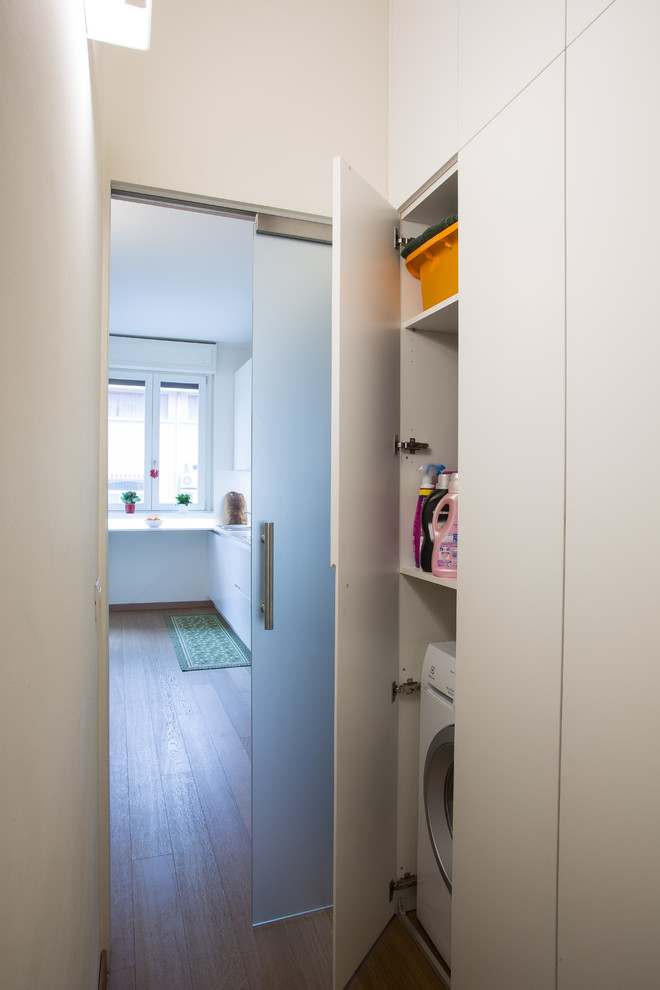 Foto di una piccola lavanderia moderna con pareti beige, parquet chiaro, lavatrice e asciugatrice nascoste e pavimento marrone