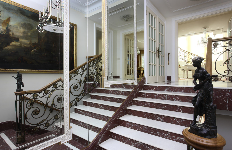 На фото: большая п-образная лестница в стиле неоклассика (современная классика) с мраморными ступенями, подступенками из мрамора и перилами из смешанных материалов