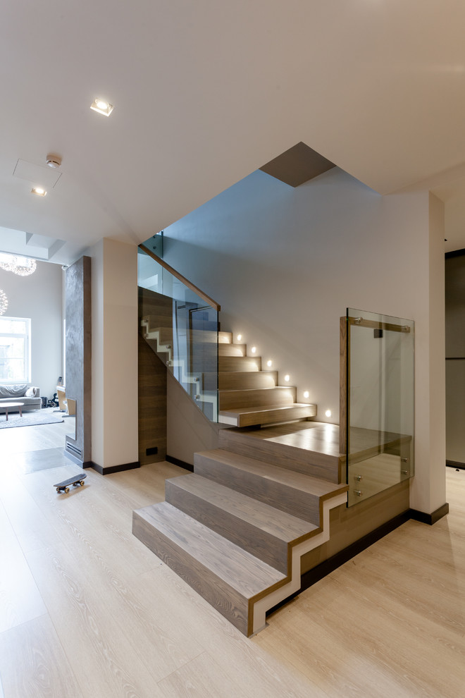 Стильный дизайн: большая угловая деревянная лестница в современном стиле с деревянными ступенями и стеклянными перилами - последний тренд