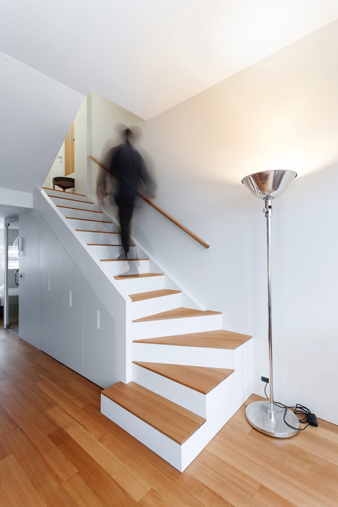 Cette photo montre un petit escalier peint courbe tendance avec des marches en bois, un garde-corps en bois et éclairage.