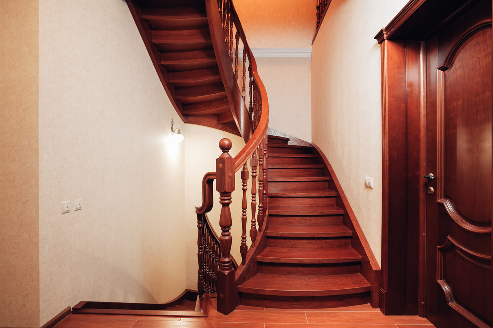 Foto de escalera curva tradicional de tamaño medio con escalones de madera, contrahuellas de madera y barandilla de madera