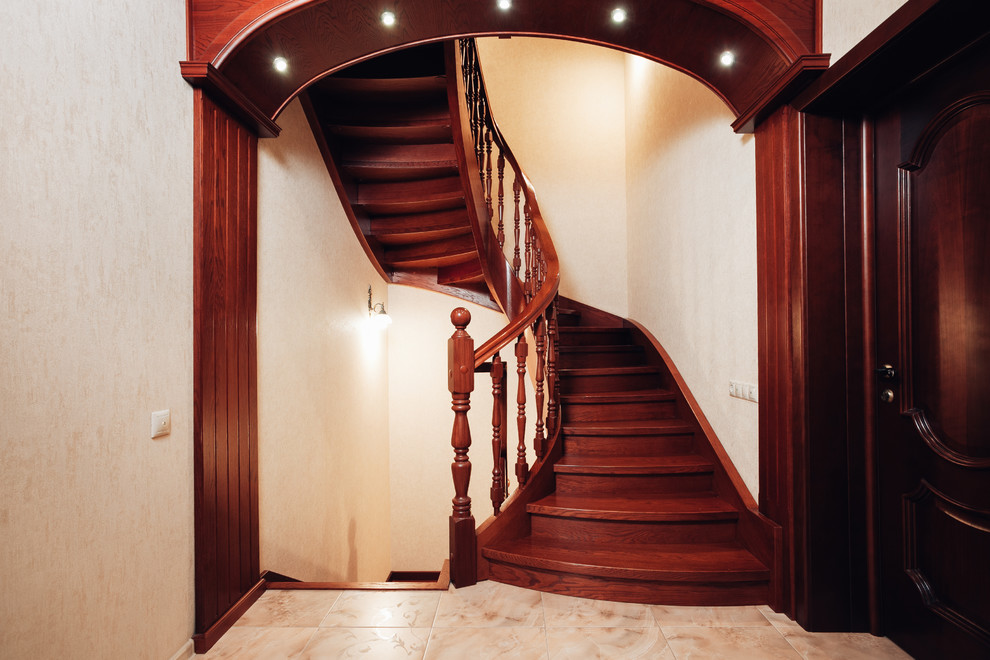 Imagen de escalera curva clásica de tamaño medio con escalones de madera, contrahuellas de madera y barandilla de madera