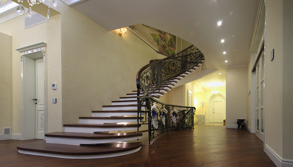 Foto de escalera curva clásica grande con escalones de madera y contrahuellas de hormigón