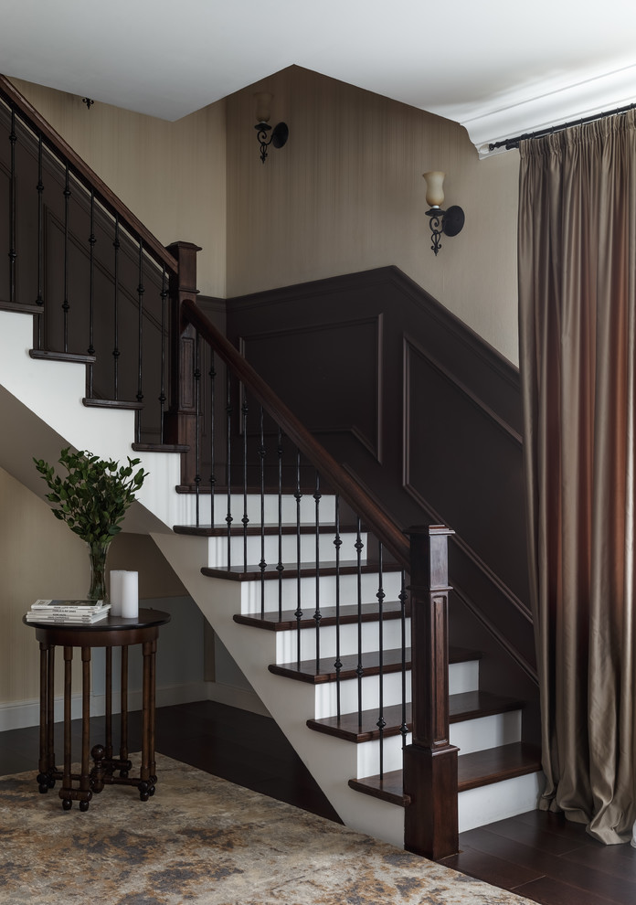 На фото: угловая лестница в классическом стиле с деревянными ступенями, крашенными деревянными подступенками и перилами из смешанных материалов