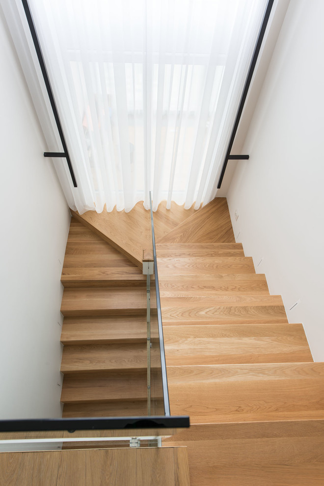 Свежая идея для дизайна: п-образная деревянная лестница среднего размера в современном стиле с деревянными ступенями и стеклянными перилами - отличное фото интерьера