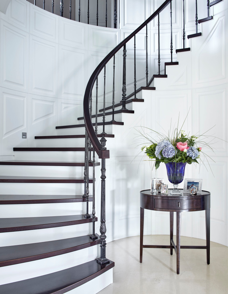 На фото: изогнутая лестница в стиле неоклассика (современная классика) с деревянными ступенями и перилами из смешанных материалов с