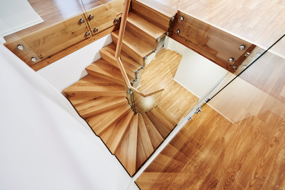 На фото: изогнутая деревянная лестница в скандинавском стиле с деревянными ступенями и перилами из смешанных материалов