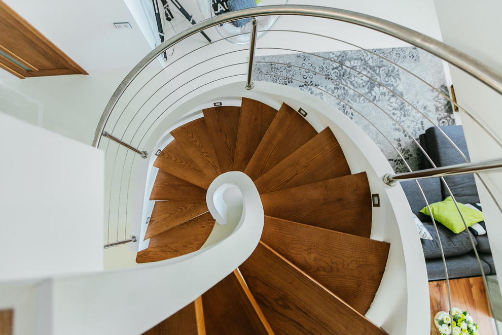 Стильный дизайн: большая винтовая лестница в современном стиле с деревянными ступенями и металлическими перилами - последний тренд
