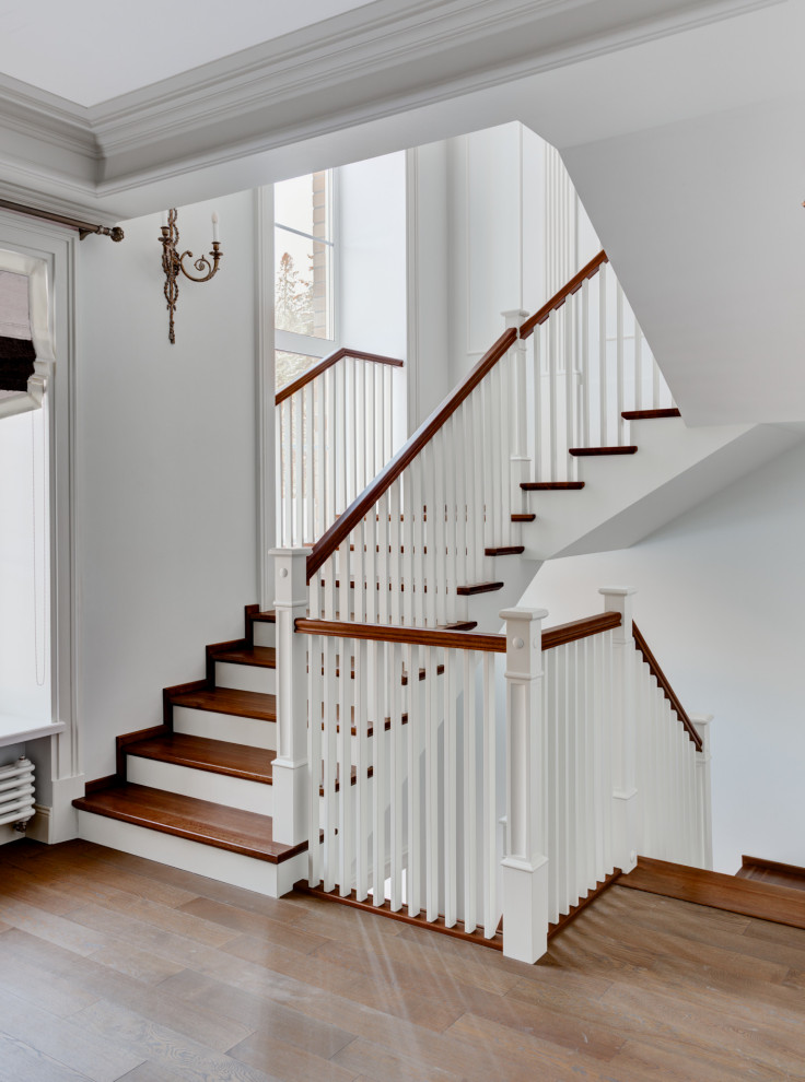 На фото: п-образная лестница в стиле неоклассика (современная классика) с деревянными ступенями и деревянными перилами с