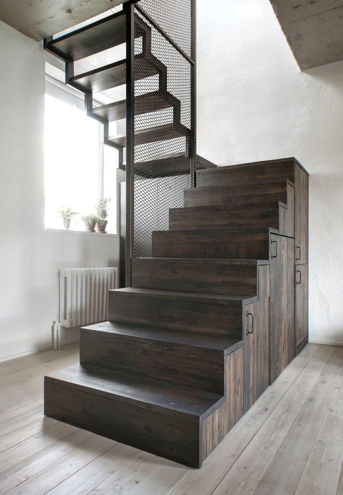 Cette photo montre un petit escalier industriel en U avec des contremarches en bois, un garde-corps en métal, des marches en bois et rangements.