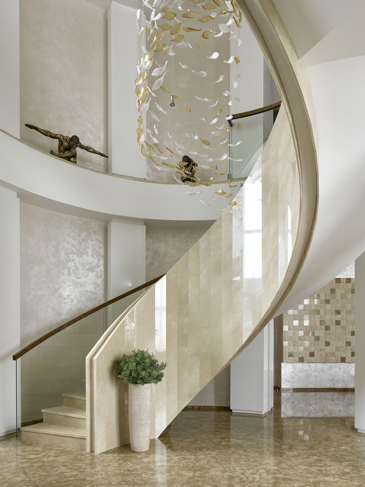 Пример оригинального дизайна: большая изогнутая лестница в современном стиле с мраморными ступенями, подступенками из мрамора и перилами из смешанных материалов