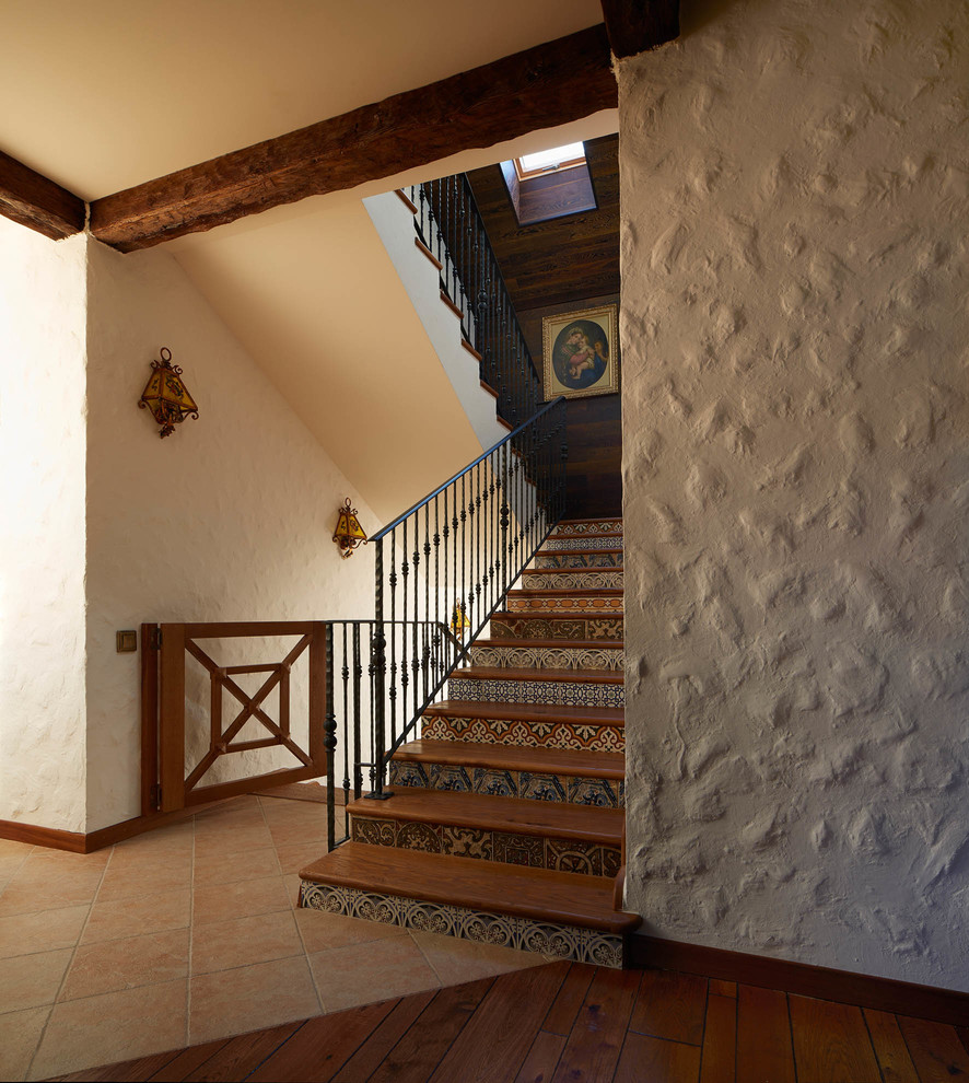 Foto de escalera en U campestre con escalones de madera, contrahuellas con baldosas y/o azulejos y barandilla de metal