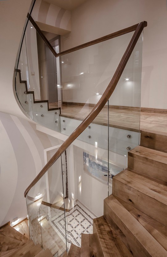 Стильный дизайн: изогнутая деревянная лестница в современном стиле с деревянными ступенями и стеклянными перилами - последний тренд