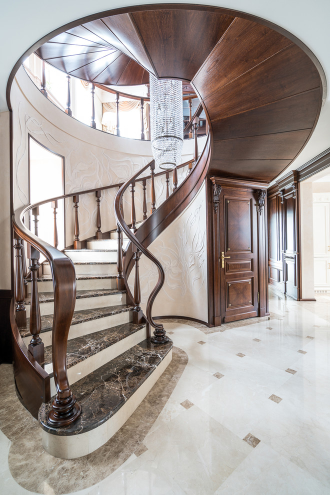 Свежая идея для дизайна: изогнутая лестница в классическом стиле с мраморными ступенями и деревянными перилами - отличное фото интерьера