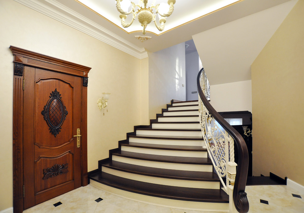 На фото: изогнутая лестница в классическом стиле с деревянными ступенями и крашенными деревянными подступенками с