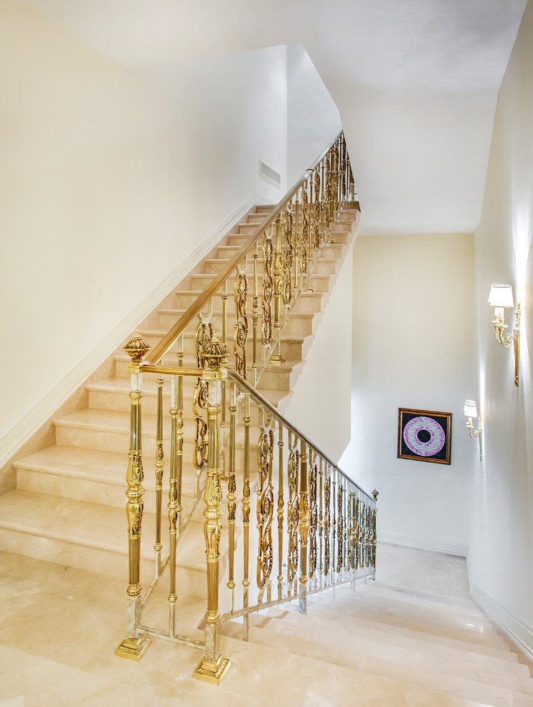Imagen de escalera en U clásica grande con escalones de mármol, contrahuellas de mármol y barandilla de metal