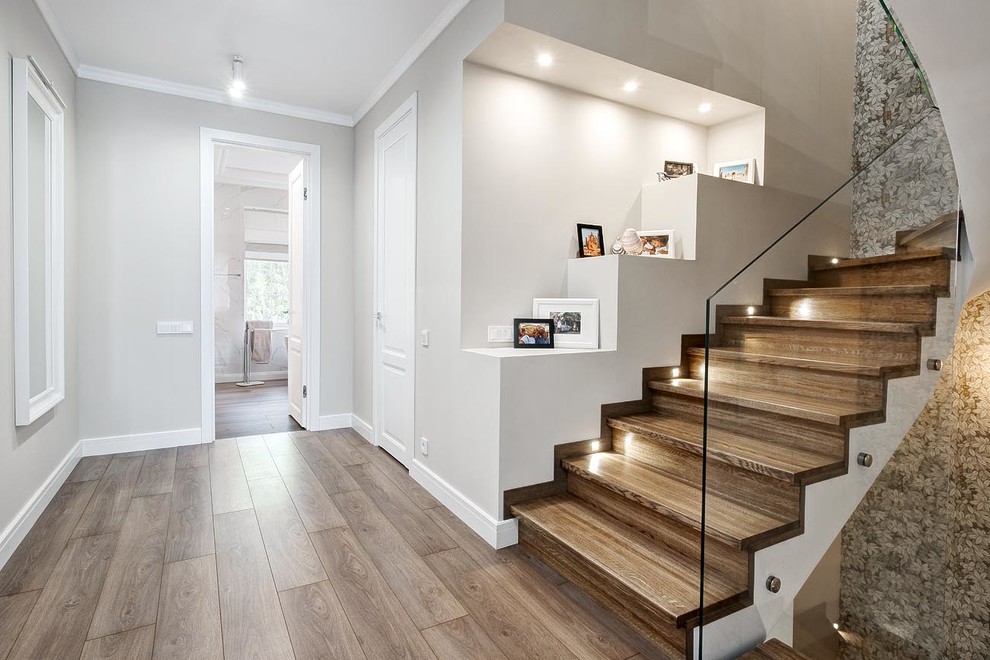 Cette photo montre un escalier courbe tendance de taille moyenne avec des marches en bois, des contremarches en bois et un garde-corps en verre.