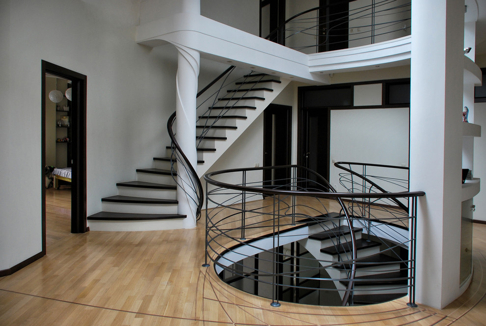 Пример оригинального дизайна: большая изогнутая металлическая лестница в современном стиле с крашенными деревянными ступенями