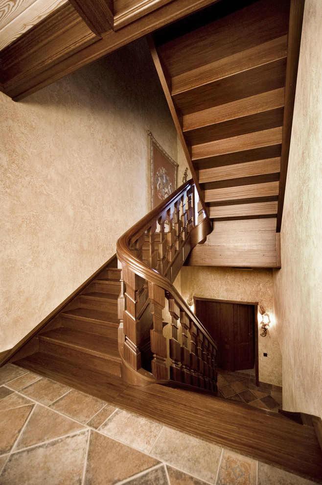 На фото: изогнутая деревянная лестница в стиле рустика с деревянными ступенями и деревянными перилами с
