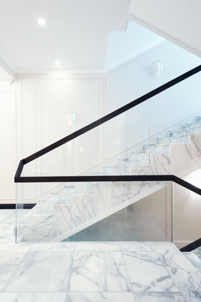 Идея дизайна: большая п-образная лестница в стиле неоклассика (современная классика) с мраморными ступенями, подступенками из мрамора и стеклянными перилами