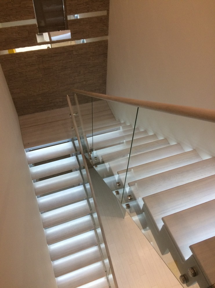 На фото: большая п-образная лестница в современном стиле с деревянными ступенями и стеклянными перилами