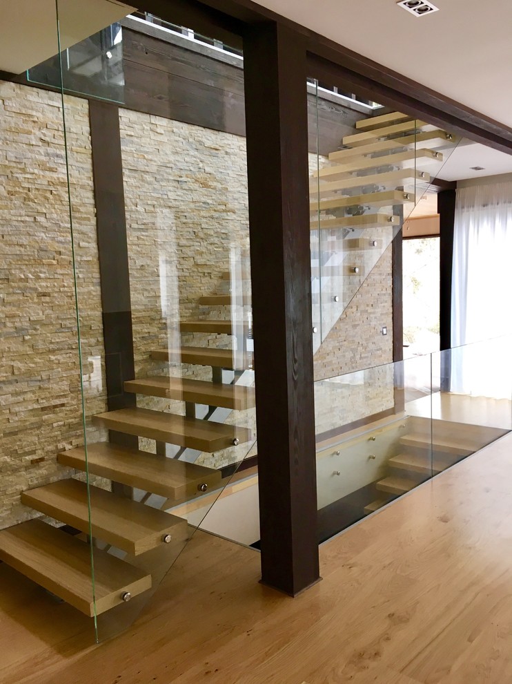 Diseño de escalera contemporánea con escalones de madera, contrahuellas de metal y barandilla de vidrio