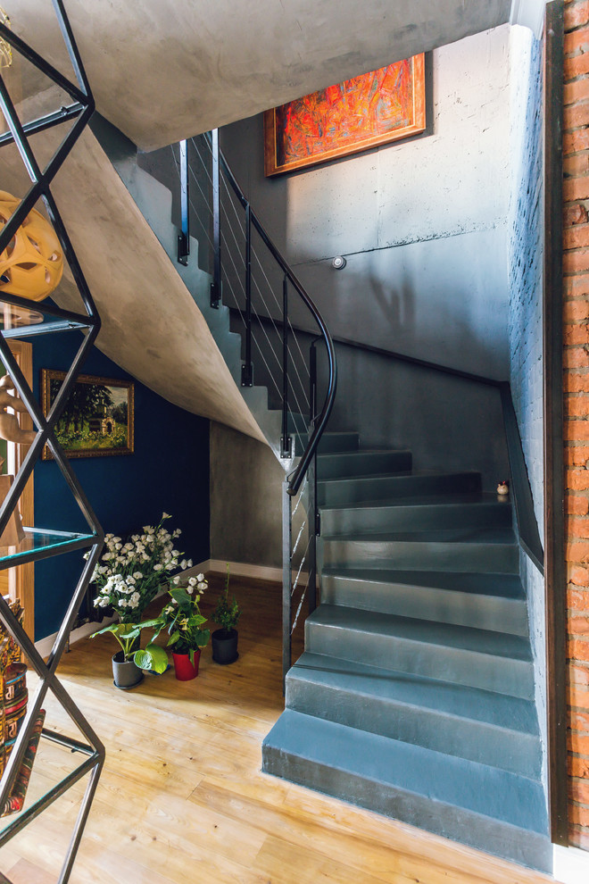 На фото: изогнутая бетонная лестница в стиле лофт с бетонными ступенями и металлическими перилами с
