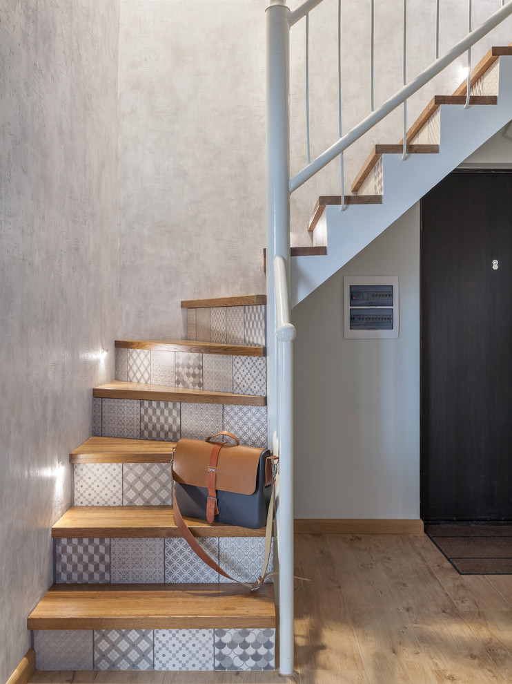 Ejemplo de escalera curva actual con escalones de madera, contrahuellas con baldosas y/o azulejos y barandilla de metal