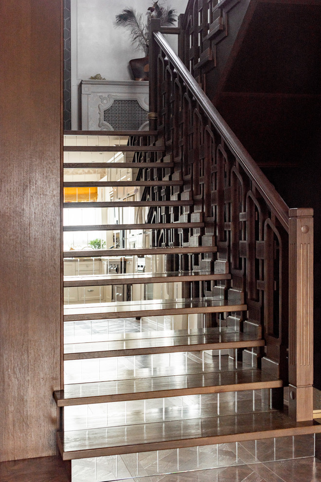 他の地域にあるトランジショナルスタイルのおしゃれな折り返し階段 (ガラスの蹴込み板、木材の手すり) の写真