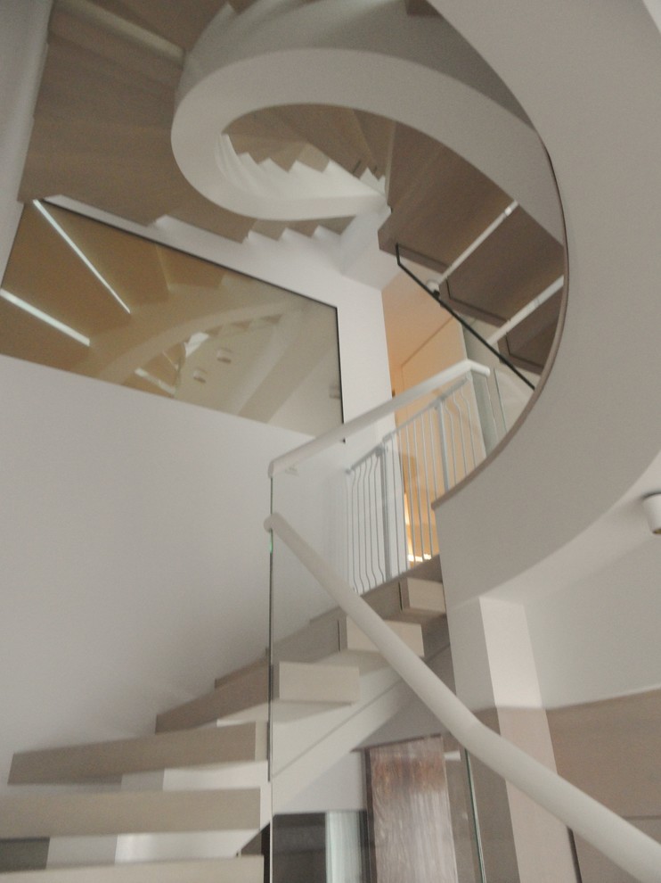 Modelo de escalera curva actual grande con escalones de madera, contrahuellas de madera y barandilla de vidrio