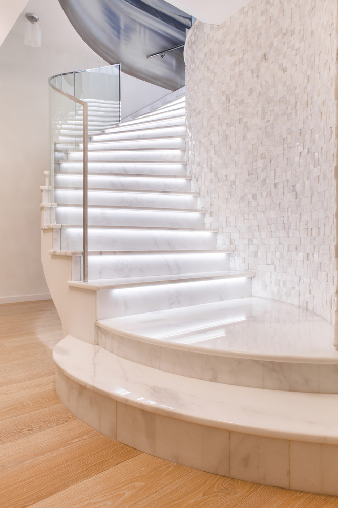 Идея дизайна: изогнутая лестница в современном стиле с мраморными ступенями, подступенками из мрамора и стеклянными перилами