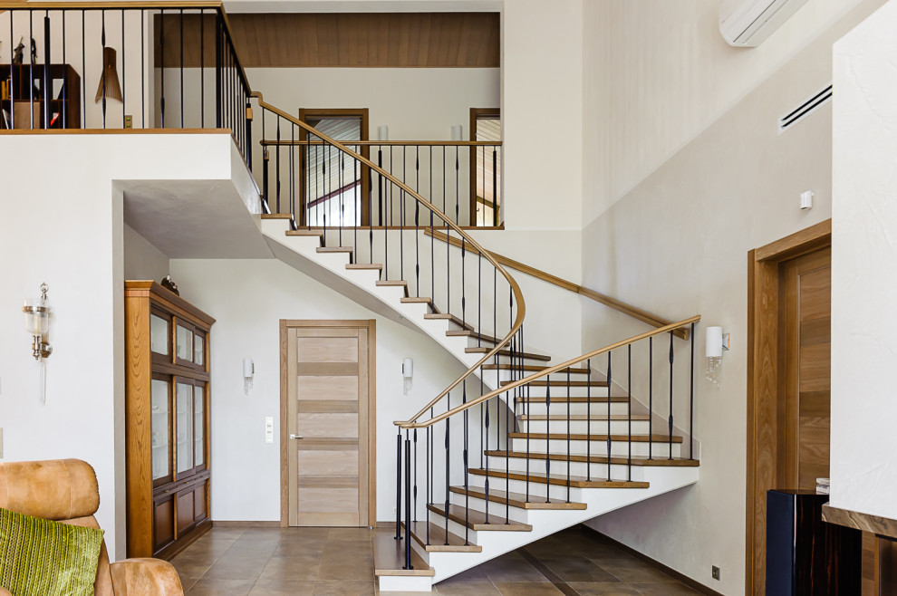 Стильный дизайн: большая изогнутая бетонная лестница в современном стиле с деревянными ступенями и перилами из смешанных материалов - последний тренд