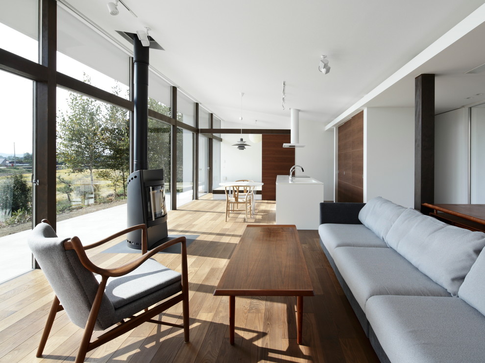 Foto di un soggiorno minimalista aperto con pareti bianche, stufa a legna, cornice del camino in pietra e pavimento marrone