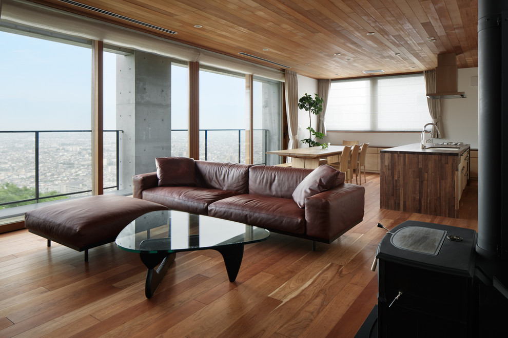 Modelo de salón para visitas abierto moderno con paredes blancas, suelo de madera en tonos medios, estufa de leña y suelo marrón