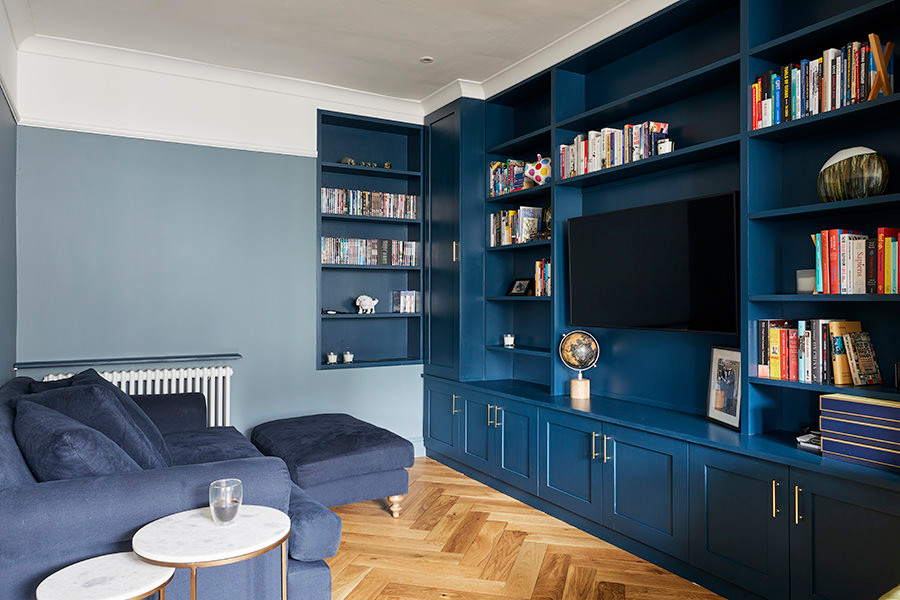 Réalisation d'un petit salon tradition fermé avec une bibliothèque ou un coin lecture, un mur bleu, un sol en bois brun, un téléviseur fixé au mur et un sol marron.