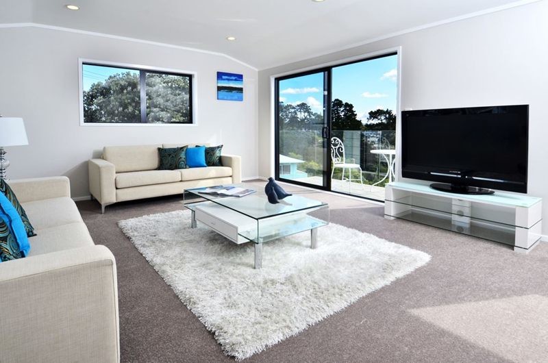 Example of a small beach style open concept carpeted living room design in Auckland with white walls and a tv stand