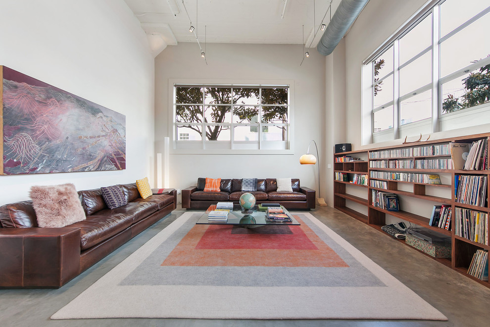 Immagine di un soggiorno industriale aperto con libreria, pareti bianche, pavimento in cemento, nessun camino, nessuna TV e tappeto